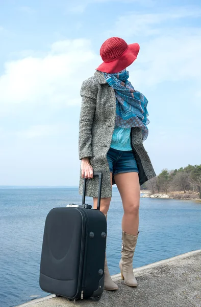 Fille dans un chapeau rouge avec une valise en face de la mer — Photo