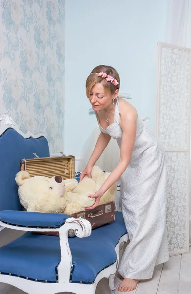 Girl in a retro style wedding dress is packing a bear toy in a s — Stock Photo, Image