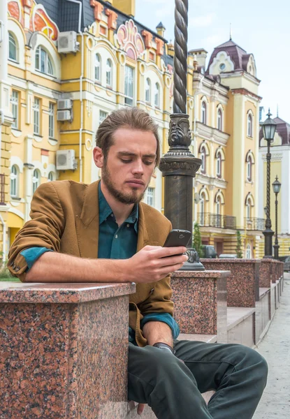 Un giovane seduto su una panchina con il cellulare — Foto Stock