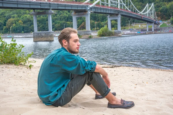 Mladý muž sedí nedaleko řeky — Stock fotografie