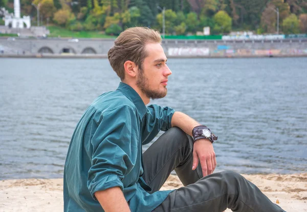 Hombre joven está sentado cerca de un río —  Fotos de Stock