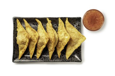 Beyaz üzerine izole edilmiş acı biber soslu siyah seramik bir tabakta servis edilen leziz kızarmış altın wonton manzarası. Asya aperatifleri ve atıştırmalık menüleri için mükemmel..