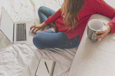 Sıcak kahve içip dizüstü bilgisayar kullanan, video izleyen, boş alan arayan Latin bir kadının portresi. Kanepede oturuyorsun ve rahat evinde dinleniyorsun. Evde yaratıcı iş kavramı. Seçici odak.