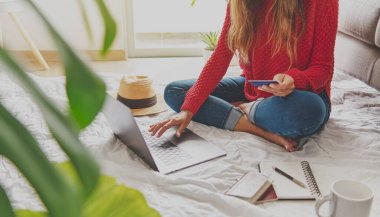 Güzel genç bayan gezgin internetten ya da uçuşta alışveriş yapıyor. Evde kredi kartıyla, manzaralı. Evde yaratıcı iş kavramı. Seçici odak.