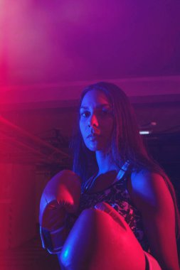 Güzel kadın boksör eğitimi, kırmızı boks eldivenleri, kırmızı ve mavi ışıklı ring, endüstriyel spor salonu. seçici odak