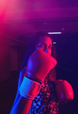 Güzel kadın boksör eğitimi, kırmızı boks eldivenleri, kırmızı ve mavi ışıklı ring, endüstriyel spor salonu. seçici odak