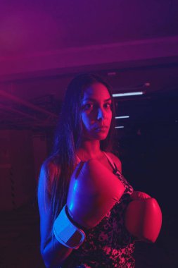 Güzel kadın boksör eğitimi, kırmızı boks eldivenleri, kırmızı ve mavi ışıklı ring, endüstriyel spor salonu. seçici odak