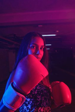 Güzel kadın boksör eğitimi, kırmızı boks eldivenleri, kırmızı ve mavi ışıklı ring, endüstriyel spor salonu. seçici odak