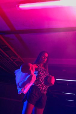 Güzel kadın boksör eğitimi, kırmızı boks eldivenleri, kırmızı ve mavi ışıklı ring, endüstriyel spor salonu. seçici odak