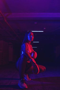 Güzel kadın boksör eğitimi, kırmızı boks eldivenleri, kırmızı ve mavi ışıklı ring, endüstriyel spor salonu, neon ışıklar. seçici odak