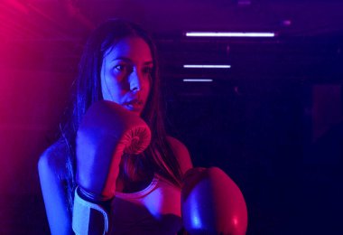Güzel kadın boksör eğitimi, kırmızı boks eldivenleri, kırmızı ve mavi ışıklı ring, endüstriyel spor salonu, neon ışıklar. seçici odak