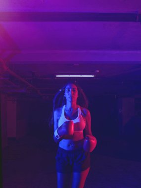 Güzel kadın boksör eğitimi, kırmızı boks eldivenleri, kırmızı ve mavi ışıklı ring, endüstriyel spor salonu, neon ışıklar. seçici odak