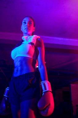 Güzel kadın boksör eğitimi, kırmızı boks eldivenleri, kırmızı ve mavi ışıklı ring, endüstriyel spor salonu, neon ışıklar. seçici odak