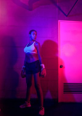 Güzel kadın boksör eğitimi, kırmızı boks eldivenleri, kırmızı ve mavi ışıklı ring, endüstriyel spor salonu, neon ışıklar. seçici odak