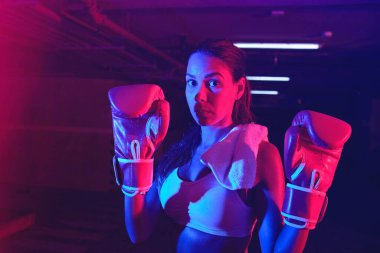 Güzel kadın boksör eğitimi, kırmızı boks eldivenleri, kırmızı ve mavi ışıklı ring, endüstriyel spor salonu, neon ışıklar. seçici odak