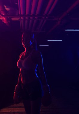 Siluet kadın boksör eğitimi, kırmızı boks eldivenleri, kırmızı ve mavi ışıklı ring, endüstriyel spor salonu, neon ışıklar. seçici odak