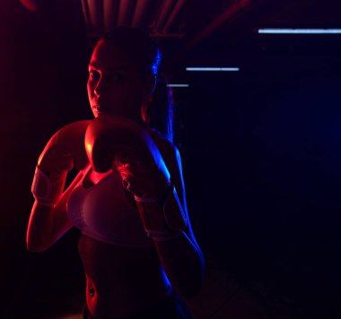 Siluet kadın boksör eğitimi, kırmızı boks eldivenleri, kırmızı ve mavi ışıklı ring, endüstriyel spor salonu, neon ışıklar. seçici odak