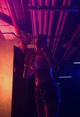 Siluet kadın boksör eğitimi, kırmızı boks eldivenleri, kırmızı ve mavi ışıklı ring, endüstriyel spor salonu, neon ışıklar. seçici odak