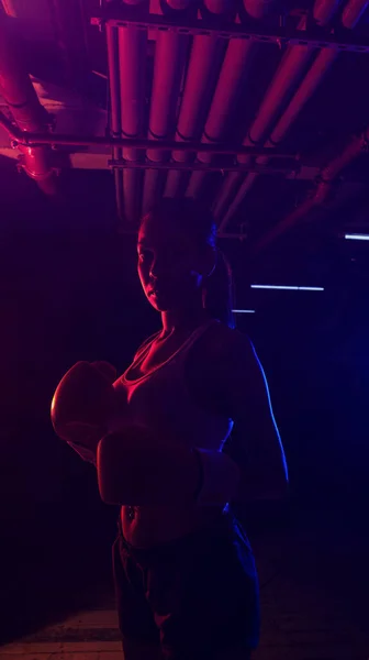 Silhouette female boxer training, red boxing gloves, ring with red and blue lights, industrial gym, neon lights. selective focus