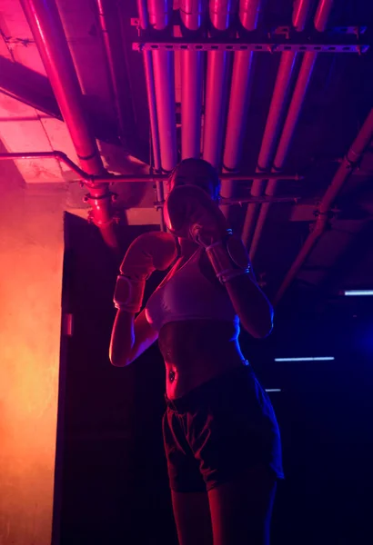 Silhouette female boxer training, red boxing gloves, ring with red and blue lights, industrial gym, neon lights. selective focus