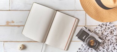 Analog bir kamera ve ahşap bir masanın üzerinde bir defter, fotoğrafçının elleri eski bir film kamerasını ahşap arka planda, seyahat kıyafetinde, konsept yolculuğunda tutuyor.