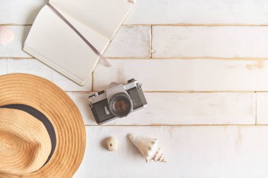 Analog bir kamera ve ahşap bir masanın üzerinde bir defter, fotoğrafçının elleri eski bir film kamerasını ahşap arka planda, seyahat kıyafetinde, konsept yolculuğunda tutuyor.