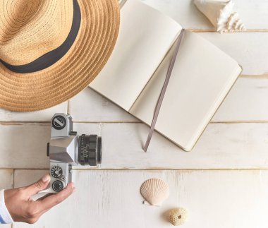 Analog bir kamera ve ahşap bir masanın üzerinde bir defter, fotoğrafçının elleri eski bir film kamerasını ahşap arka planda, seyahat kıyafetinde, konsept yolculuğunda tutuyor.