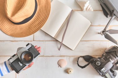 Analog bir kamera ve ahşap bir masanın üzerinde bir defter, fotoğrafçının elleri eski bir film kamerasını ahşap arka planda, seyahat kıyafetinde, konsept yolculuğunda tutuyor.
