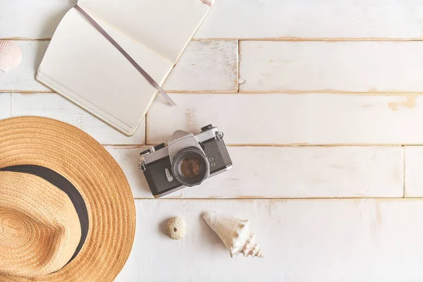 Analog bir kamera ve ahşap bir masanın üzerinde bir defter, fotoğrafçının elleri eski bir film kamerasını ahşap arka planda, seyahat kıyafetinde, konsept yolculuğunda tutuyor.