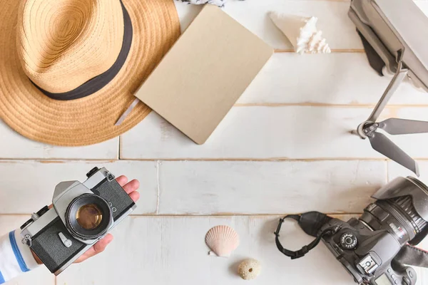 Top view of an analog camera and a notebook on a wooden table, photographer's hands hold old film camera on wooden background, travel outfit, concept travel