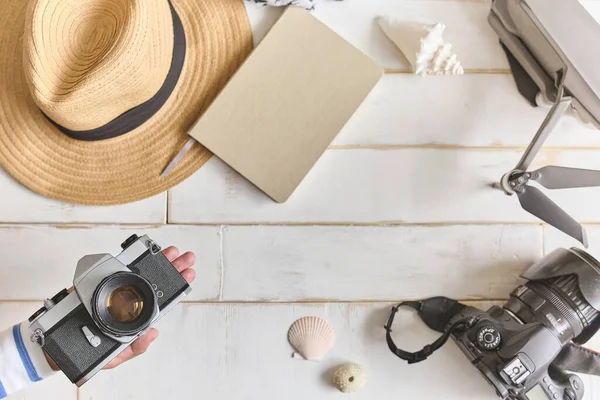 Analog bir kamera ve ahşap bir masanın üzerinde bir defter, fotoğrafçının elleri eski bir film kamerasını ahşap arka planda, seyahat kıyafetinde, konsept yolculuğunda tutuyor.