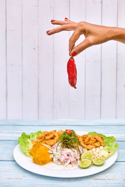 Woman holding handful of red chillies, mid section, close-up ,hands with spicy red chili pepper and ceviche background, Peruvian hot red chili Aji Limo, Peruvian ingredients