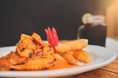 Peru yemeği: Peru yemeği: Maço bir balık, ahşap masa, beyaz bir tabakta servis ediliyor, deniz ürünleri sosunda kızartılan balık, yanında patates, deniz ürünü, pirinç ve mor mısır suyu.