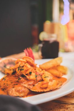 Peru yemeği: Peru yemeği: Maço bir balık, ahşap masa, beyaz bir tabakta servis ediliyor, deniz ürünleri sosunda kızartılan balık, yanında patates, deniz ürünü, pirinç ve mor mısır suyu.