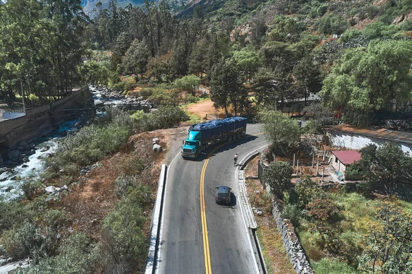 Professional cyclist training on the road with safety escort car. Cyclist followed by team car. Selective focus. Matucana, Peru. Aerial view.