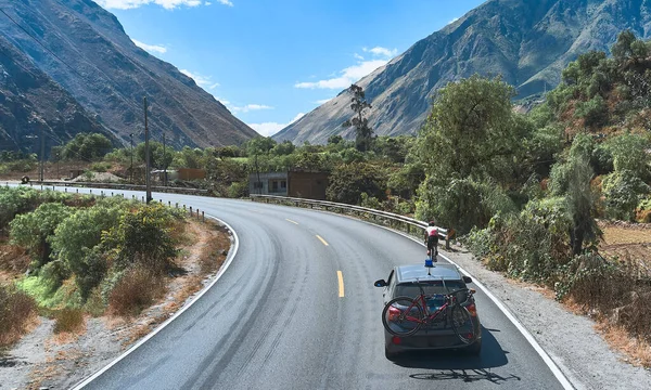 Professional cyclist training on the road with safety escort car. Cyclist followed by team car. Selective focus. Matucana, Peru. Aerial view.