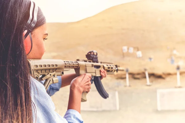 Mulher com poder de tiro apontando rifle de assalto ao alvo. Foco seletivo — Fotografia de Stock