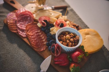 Şarküteri tahtası gri bir paspasın üzerinde sunuluyor. Atıştırma partisi için çeşitli aperatifler sunuluyor.