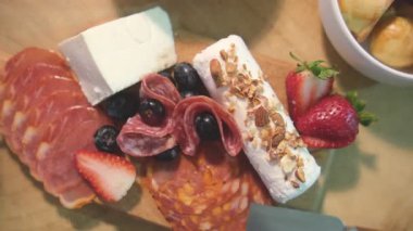 Şarküteri tahtası dilimlenmiş et, peynir, meyve ve fındık sunar.