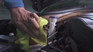 Profesyonel tamirci ön cam temizleme sıvısını doldurarak araba bakımı yapıyor.
