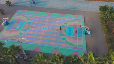 Arkadaşların halka açık bir parkta renkli bir sahada basketbol oynamalarının havadan görünüşü