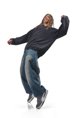 Rastalı genç adam hip hop kıyafetleriyle dans ediyor, bir gülümsemeyle duraksama hareketi yapıyor.