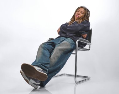 Kollarını kavuşturmuş bir sandalyede hımbıl hımbıl yürüyen genç bir erkek, ilgisizliğini yansıtıyor.