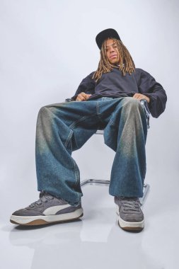 Sandalyesinde oturan rastalı ve bol kotlu genç adam şehir modasını sergiliyor.