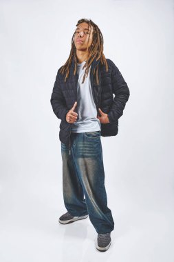 Rastalı ve bol kotlu genç bir adam stüdyoda güven içinde poz veriyor.