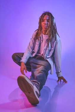 Rastalı genç adam neon ışıklı stüdyoda kulaklıkla müzik dinliyor.