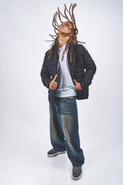 Rasta saçlı genç adam gözleri kapalı, beyaz arka planda izole bir şekilde mutlu bir şekilde dans ediyor.