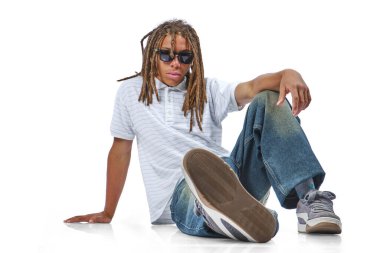 Rasta saçlı, güneş gözlüklü, beyaz arka planda oturan genç bir adam.