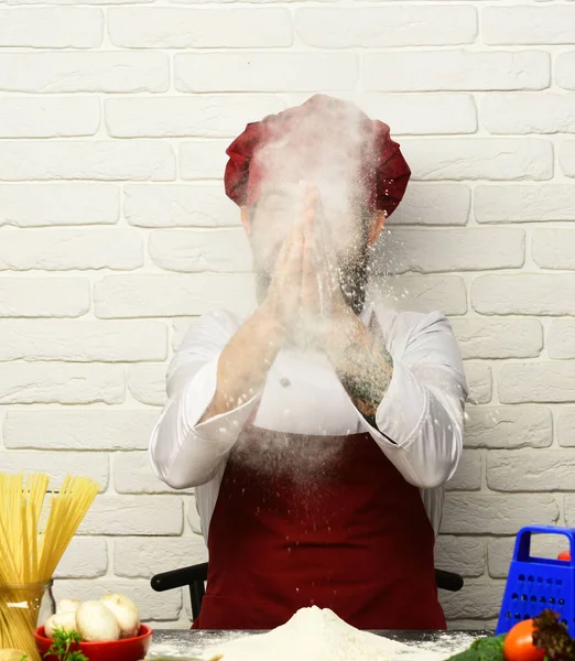 Vaření se skrytou tváří v burgundské uniformě sedí u stolu — Stock fotografie