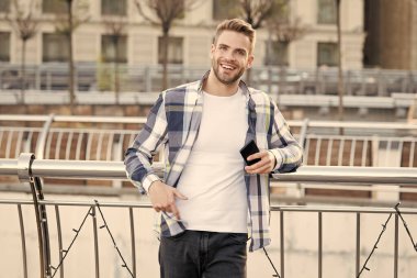 Kareli gömlek giyen bir adam. Öğrenci caddedeki ofisin yakınında modern akıllı telefon kullanıyor. Cep telefonu tutan genç iş adamının portresi. Akıllı telefon kullanan genç bir şehirli profesyonel. Taşınabilir ofis